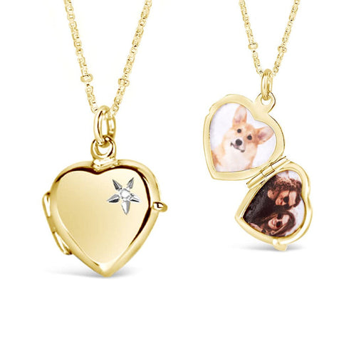 A gold heart-shaped locket with a diamond on the front, opened to show two photos of a dog and a person on a white background