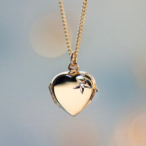 Gold heart-shaped locket with a real diamond set in a star design on a blurred pale grey background.