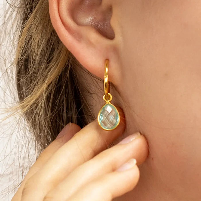 Gold hoop earring with blue topaz drop gemstone, worn on model