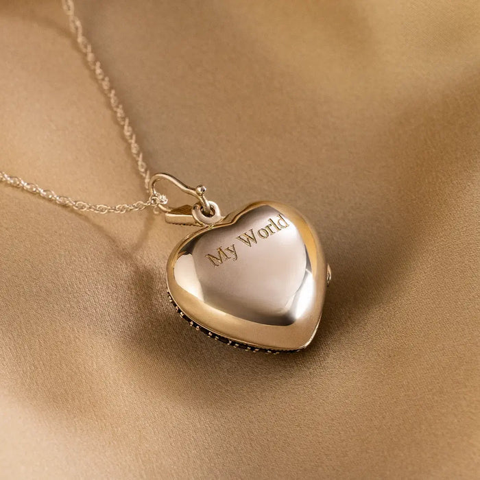 Two-tone heart locket necklace engraved with “My World,” featuring a polished silver centre and gold border, displayed on soft satin fabric.