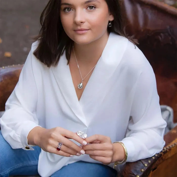 Woman wearing sterling silver chick egg locket necklace styled with white blouse and layered jewellery