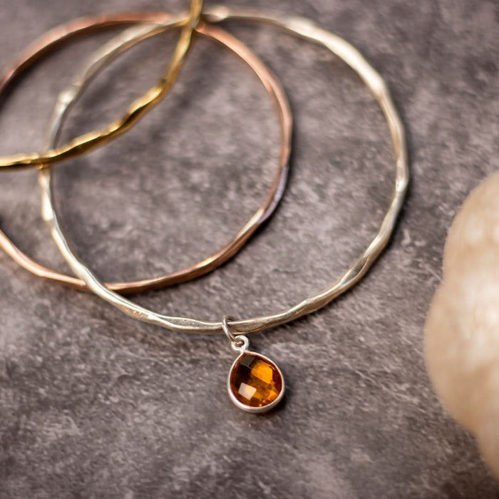 close up of three charm bangles in gold, silver and rose gold on a piece of grey fabric