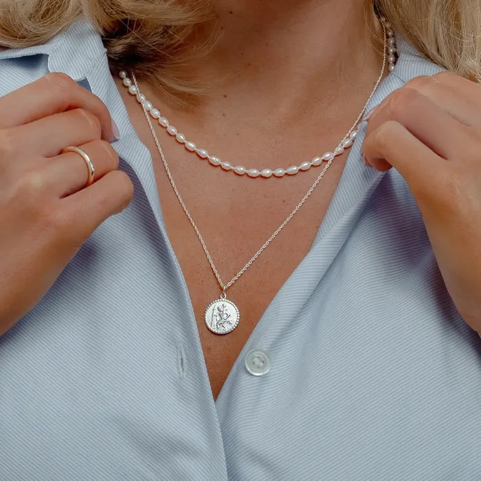 Woman wearing a dainty sterling silver St Christopher pendant with a freshwater pearl choker.