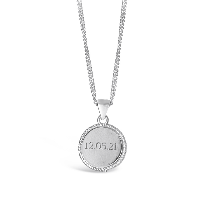 A sterling silver disc pendant necklace with the date '12.05.21' engraved on it, displayed on a chain.