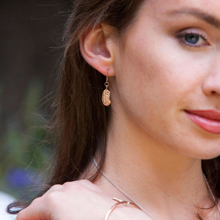 close up of model wearing feather earrings in gold