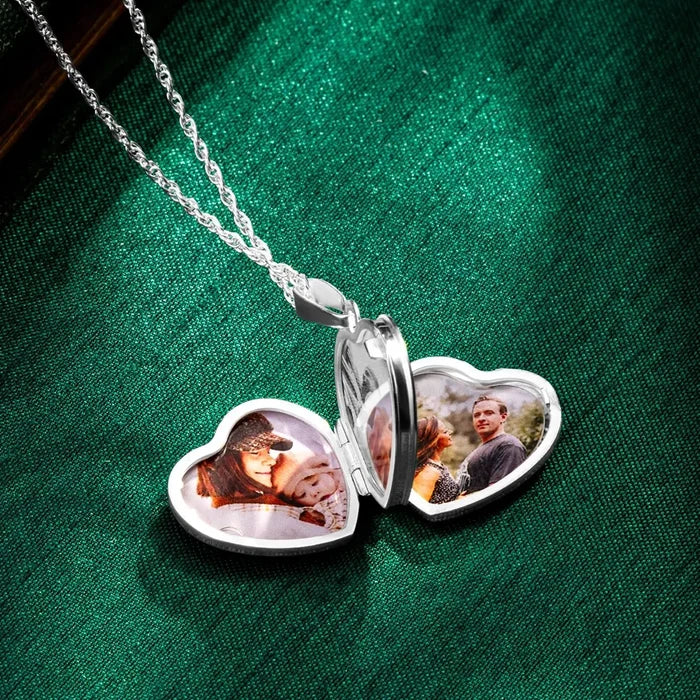 Open sterling silver heart locket necklace resting on green satin fabric, showing four personalised photo compartments inside the heart-shaped pendant.