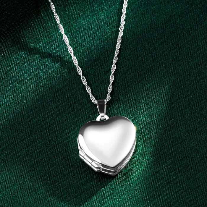 Sterling silver heart locket necklace on a delicate chain, photographed on rich green silk fabric with the polished heart pendant closed.