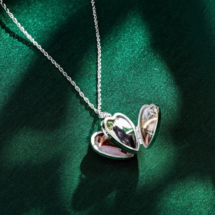 Open sterling silver heart locket necklace resting on green satin fabric, showing four personalised photo compartments inside the heart-shaped pendant.
