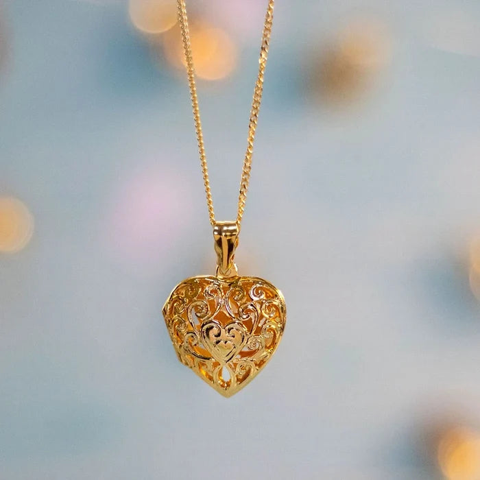 Gold filigree heart locket necklace hanging on a gold chain, against a blue background