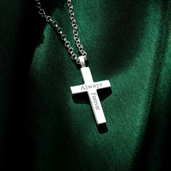 A silver cross pendant engraved with the words “Always” and “Forever,” hanging from a silver chain and resting on rich green fabric with contrasting highlights and shadows. By Lily Blanche.
