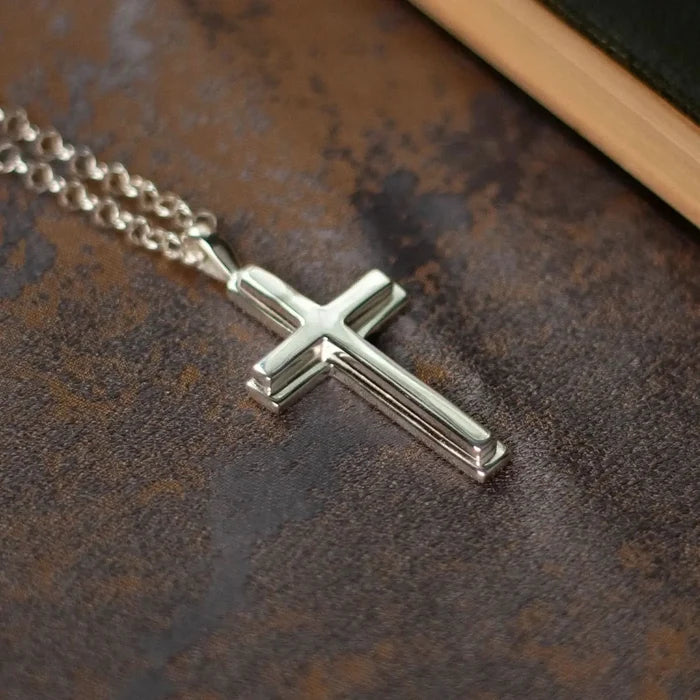 photograph of a heavy weight silver cross necklace on a belcher chain, lying against a piece of fabric