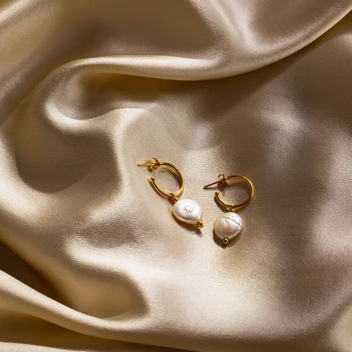 Pair of gold coin pearl hoop earrings displayed on gold satin fabric, highlighting pearl lustre and texture