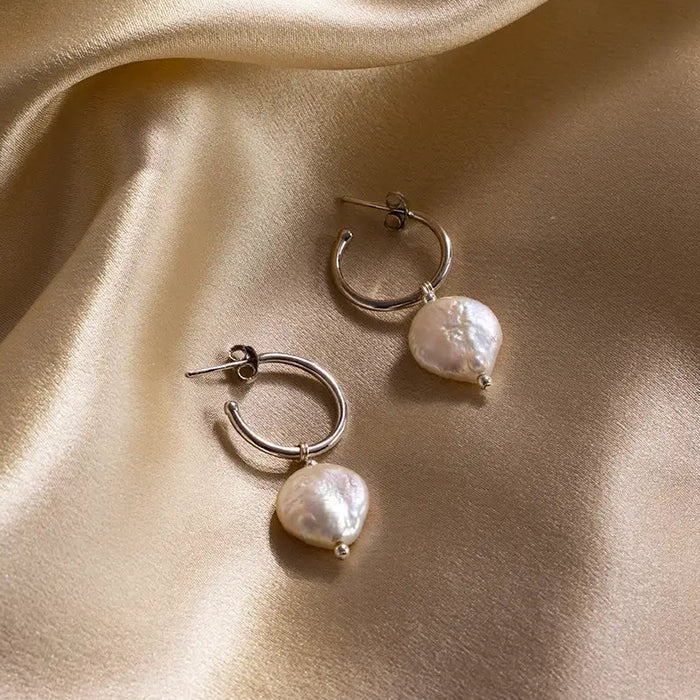 Pair of silver coin pearl hoop earrings displayed on gold satin fabric, highlighting lustre and texture