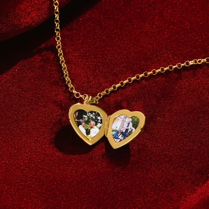 An open gold heart-shaped locket, by Lily Blanche, resting on red velvet, showing two small photos inside—each framed by the heart-shaped interior. The gold chain lies gracefully around the locket.