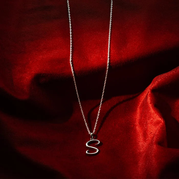 Sterling silver initial S pendant necklace on fine chain, styled on red satin background