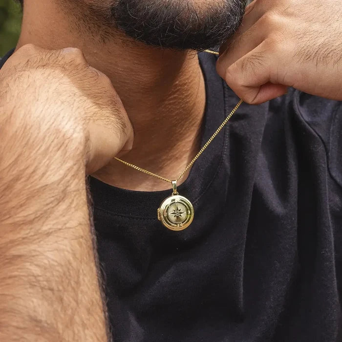Men’s gold compass locket necklace worn on chain, styled close to neck with casual black top