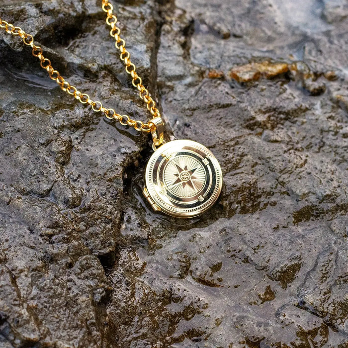 Gold compass locket necklace resting on wet rock surface, highlighting water-resistant design and shine