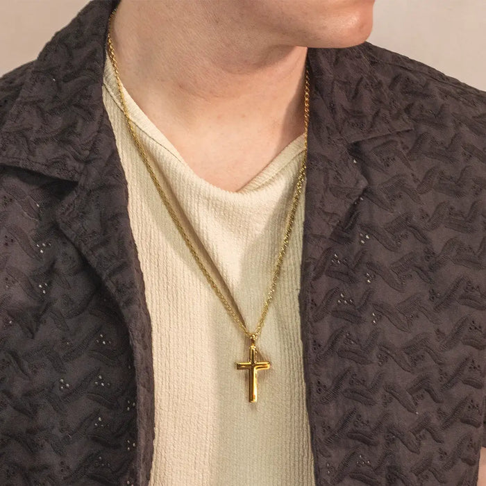 Close-up of a person wearing a heavy gold cross pendant necklace by Lily Blanche styled with a textured shirt and dark jacket