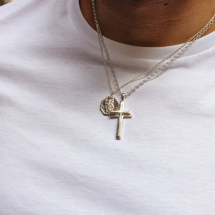 Sterling silver cross pendant necklace layered with St Christopher pendant on chains, worn by male model. By Lily Blanche.