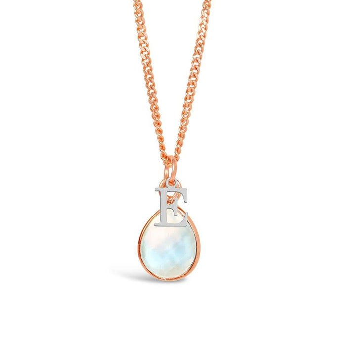 A natural moonstone charm necklace in a rose gold setting with a silver initial charm - letter E - hanging from a rose gold curb chain, photographed on a white background.