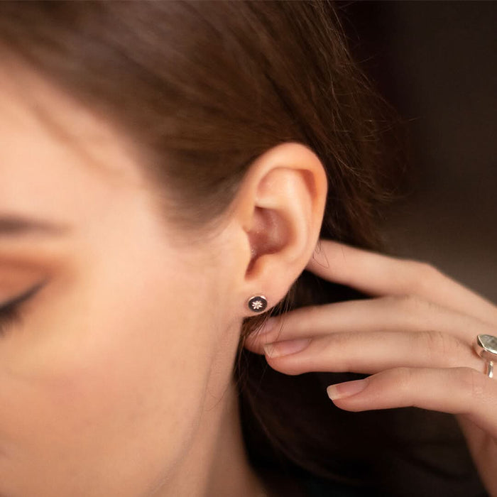 a female model wearing silver circular shaped stud earrings with a diamond decoration