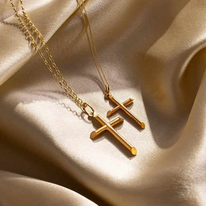 Two solid gold cross pendant necklaces on textured gold satin background, polished finish and fine chains