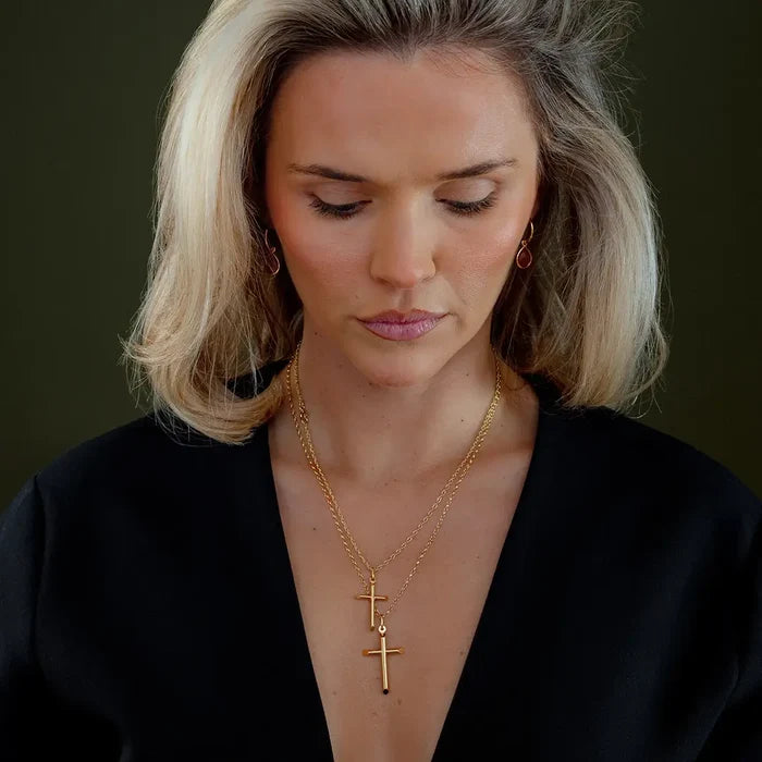 Model wearing layered gold cross pendant necklaces in small and large sizes on fine chains, styled with black outfit and minimal jewellery